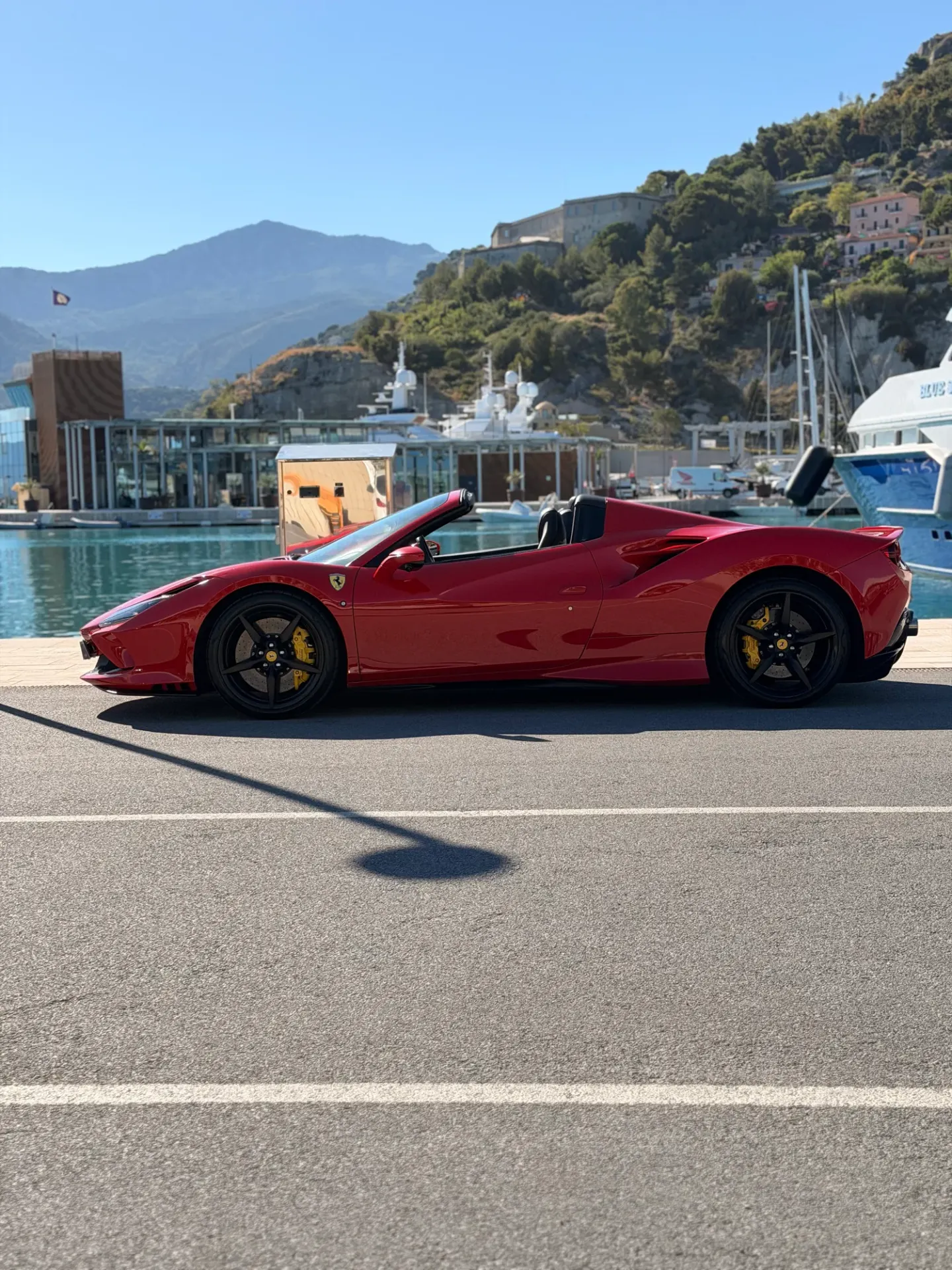 Ferrari F8 rossa vista di profilo accanto agli yacht in un porto turistico.
