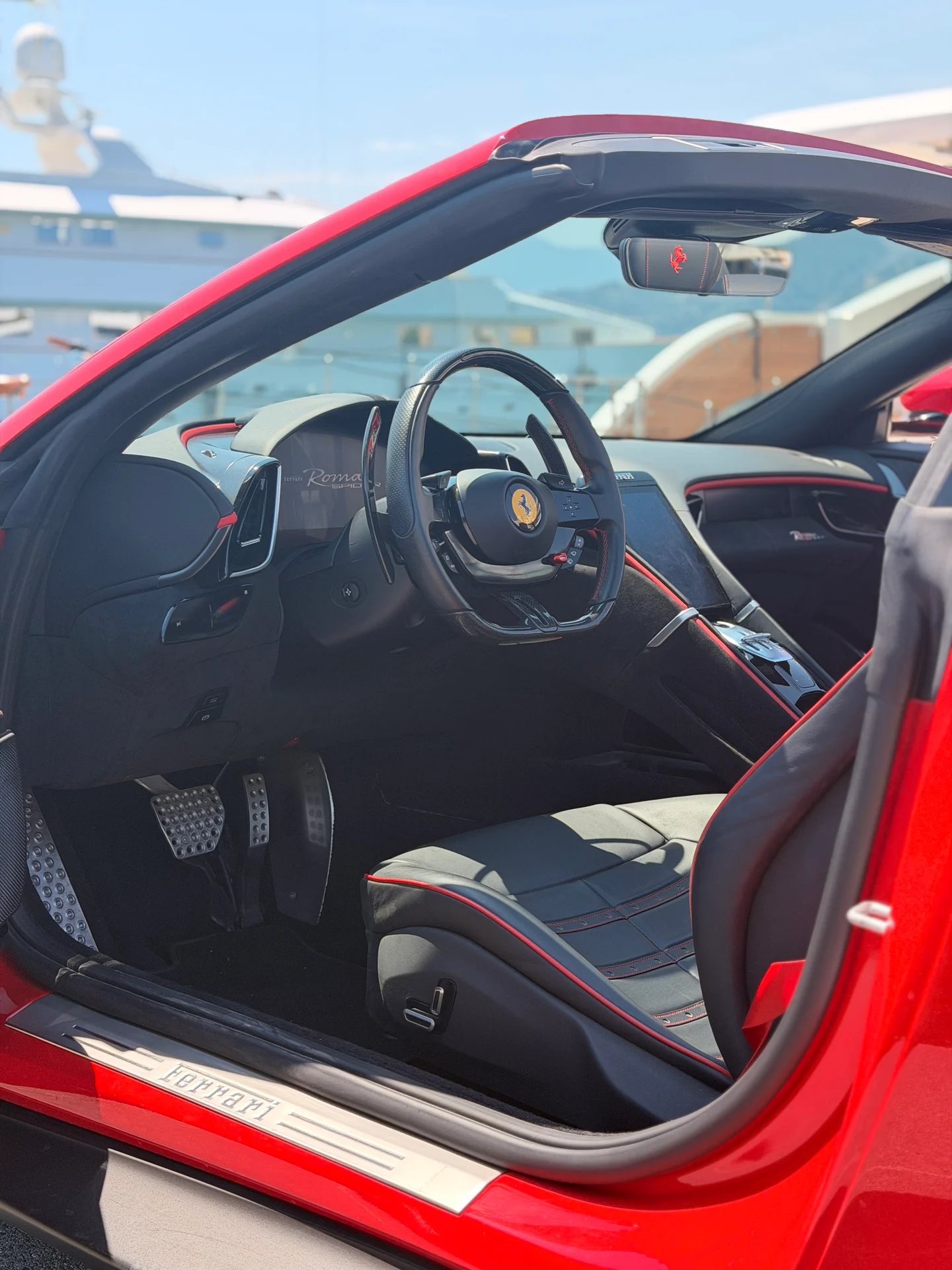 Abitacolo scuro della Ferrari Roma Spider con volante, console centrale e accenti rossi sul sedile.